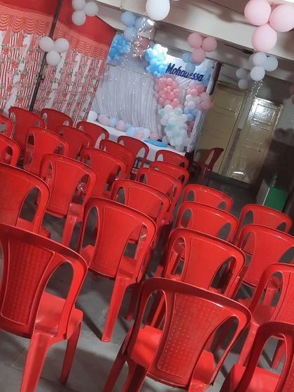 A simple birthday setup with a pastel balloon backdrop. The red chairs provide a pop of color in the hall.