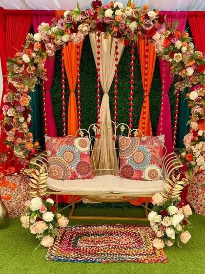 This is a beautiful bohemian-themed Mehndi decor idea. The setup uses printed cushions, a colorful rug, and a mix of floral and fabric elements for a relaxed and stylish vibe.