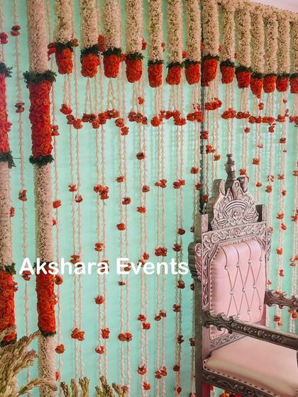 This backdrop features columns of red marigolds and strings of white jasmine against a light green curtain. The ornate silver chair provides a regal focal point for the ceremony.