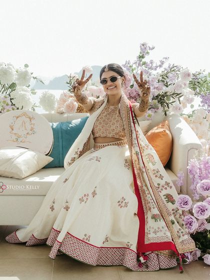 The bride shows off her completed Mehendi with a victory sign, seated on a beautifully decorated couch overlooking the Vietnamese coast.
