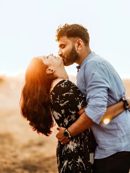 The golden hour is a magical time for photography. Here, the warm, setting sun creates a beautiful flare, highlighting the couple's intimate kiss and turning a simple moment in a field into something truly cinematic and unforgettable.