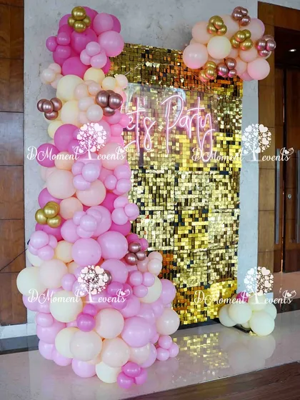 A glamorous photo booth for a Boho Rainbow-themed Annaprashan ceremony. A pink and gold balloon arrangement cascades down a shimmering gold sequin wall with a "Let's Party" neon sign.