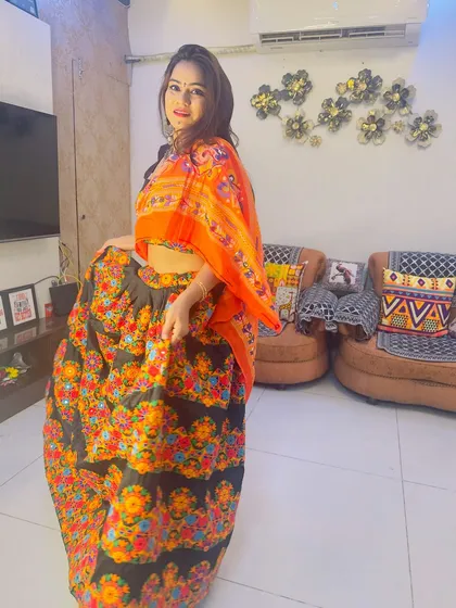 A client ready for Dandiya in a black lehenga with colorful floral embroidery, paired with a bright orange dupatta.