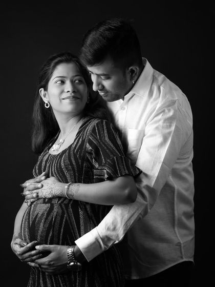 A classic black and white portrait that emphasizes emotion. The focus is entirely on the couple's loving gaze and the protective embrace around the baby bump.