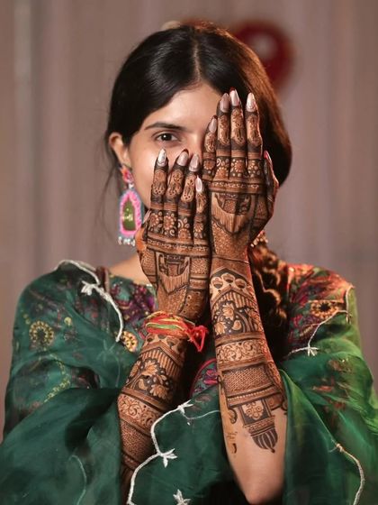 A beautiful bride showing a glimpse of her eyes through her mehandi-covered hands. A classic and elegant pose.