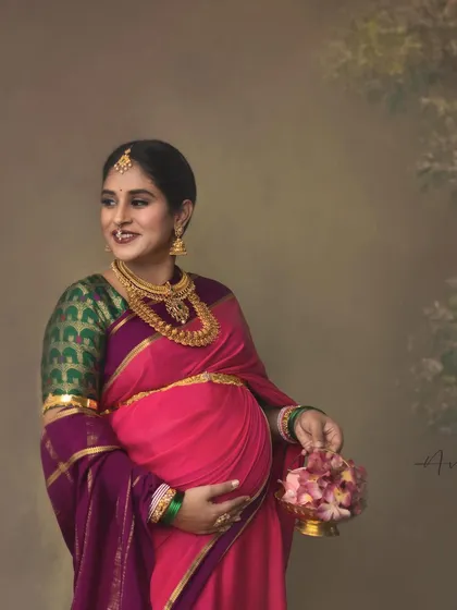 Pretty in pink, this mother-to-be glows in a vibrant saree against a soft, painterly background. The image captures a moment of happy anticipation, styled with beautiful traditional jewelry.
