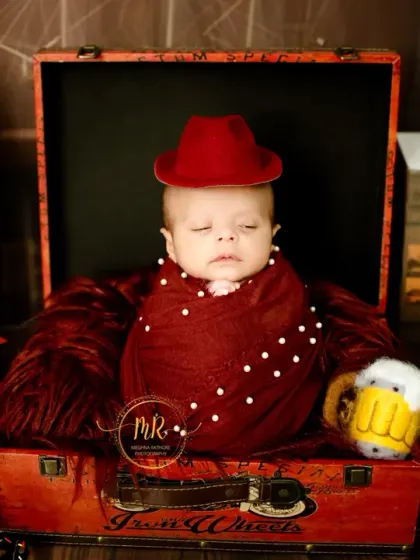 A creative newborn portrait with a vintage travel theme, featuring the baby in a suitcase with props like a globe, old books, and a toy airplane.