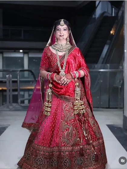 A regal bride in a deep red velvet lehenga. This outfit features elaborate embroidery on the skirt and blouse, paired with a full set of bridal jewellery, perfect for a traditional wedding ceremony.