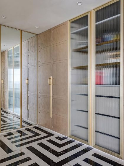 This premium walk-in area features a mix of mirrored, textured, and fluted glass wardrobe doors. The monochrome inlay flooring adds a bold graphic element to the luxurious space.