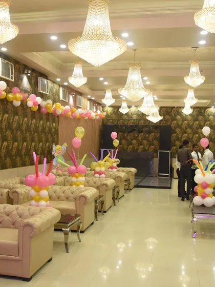 The seating area of a banquet hall decorated with balloon garlands on the walls and candy-themed balloon centerpieces on the tables.
