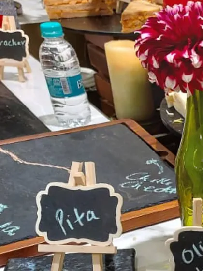 A close-up of the details at a wine and cheese event. The mini chalkboard labels for "Pita" and different cheeses add a charming and informative touch to the spread.
