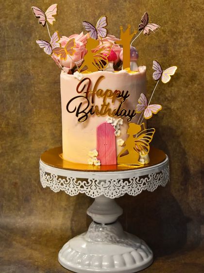 A magical fairy-themed birthday cake. This enchanting design features a pink fairy door, edible mushrooms, and delicate golden fairy and butterfly silhouettes.
