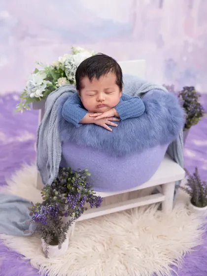 A peaceful slumber in a lavender-themed setup. This newborn rests in a purple basket, surrounded by soft fabrics and floral accents, creating a serene and colorful composition.