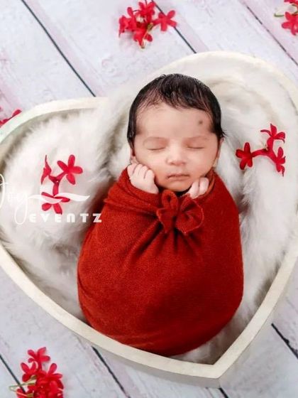 A lovely heart-themed newborn photo. The baby is wrapped in a crimson red swaddle and placed inside a white, heart-shaped bowl, creating a perfect portrait to celebrate your new love.