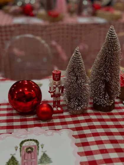 A close-up of the Christmas tablescape, featuring a red gingham runner, miniature nutcrackers, and frosted bottle brush trees for a classic holiday feel.