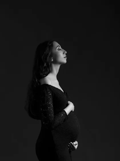 A serene solo portrait in black and white. The focus is entirely on her peaceful expression and the beautiful shape of her pregnancy.