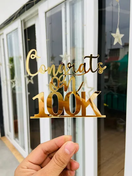 The "Congrats on 100K" topper held up, showing its bold font and celebratory design.
