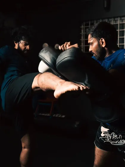 A fighter throws a powerful kick into the pads held by a coach.