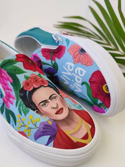 A tribute to the iconic artist Frida Kahlo, hand-painted on a pair of classic Vans slip-ons. Her portrait is surrounded by the vibrant flowers she is famous for.