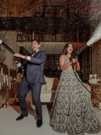 A reception moment that’s all about fun. The bride and groom take charge of the confetti cannons, their joyful expressions showing they are having the time of their lives.