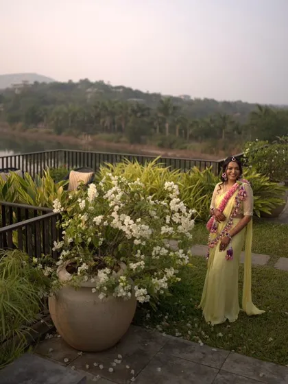 A wide shot of the bride at her beautiful lakeside Haldi venue. Our floral jewellery was designed to complement both her outfit and the scenic backdrop.