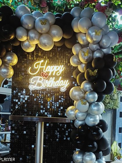 A close-up of the black and silver balloon arch with delicate butterfly details. The 'Happy Birthday' neon sign adds a warm glow, making the setup feel personal and special.