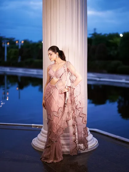 The blush pink sari captured against a twilight sky, highlighting its romantic silhouette and the intricate detailing along the borders.