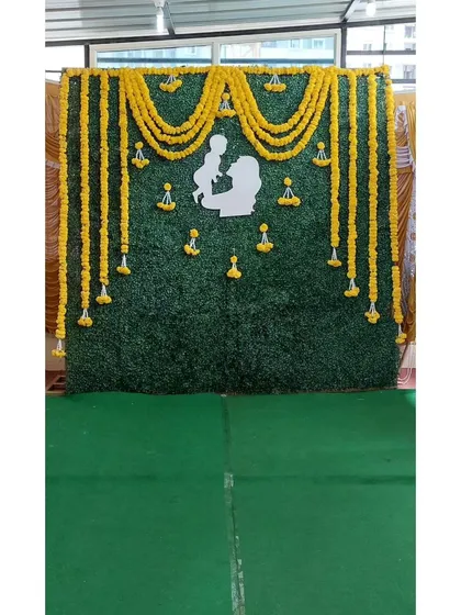 This traditional backdrop is perfect for a baby shower or naming ceremony. It features an artificial green wall decorated with bright yellow marigold garlands and a beautiful white silhouette cutout of a mother and baby.