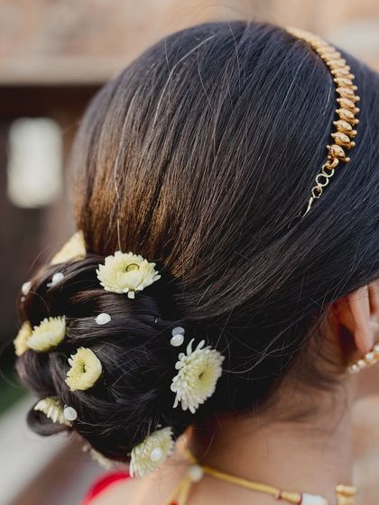 A close-up of the delicate floral bun. We tucked in dainty flowers to complement her red saree and add a touch of softness to the traditional hairstyle.
