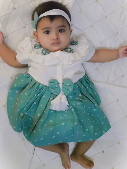 A full-body shot of my niece lying on a white quilted surface, giving a clear view of her cute green and white dress. This type of shot is great for capturing milestones.