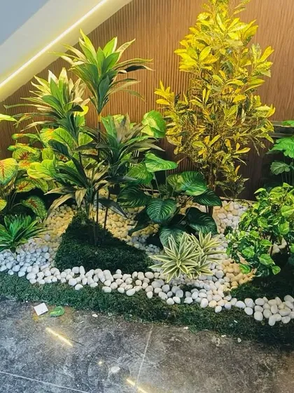 A small indoor garden bed created in a corner, using a variety of artificial plants and white pebbles for a clean, modern look.