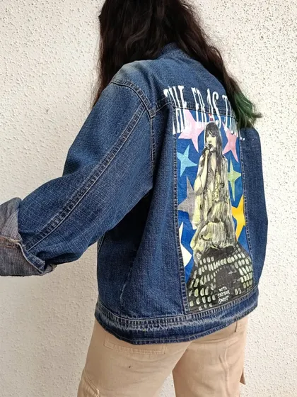 For all the Swifties, this is a hand-painted denim jacket celebrating Taylor Swift's Eras Tour. The design features a portrait of Taylor against a backdrop of colorful stars, capturing the energy of her iconic tour. This piece is a perfect way to show your love for her music.
