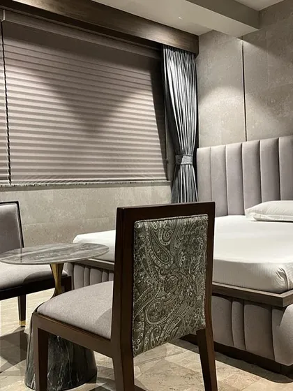 A quiet seating nook within a luxury bedroom in Juhu. The combination of a plush, channel-tufted bed, textured walls, and a chair with classic paisley upholstery creates a layered and sophisticated design.
