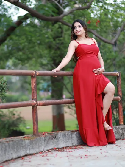 A solo portrait during an outdoor maternity shoot. The vibrant red gown stands out beautifully against the natural backdrop, creating a powerful and serene image of the mother-to-be.