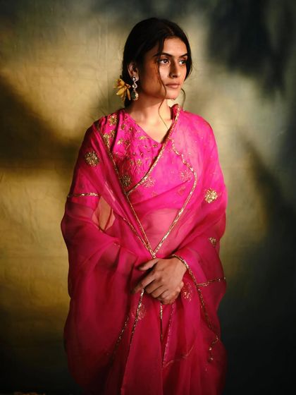 A model wrapped in a sheer pink organza dupatta, part of a beautiful saree set, highlighting the delicate fabric and gold embroidery.