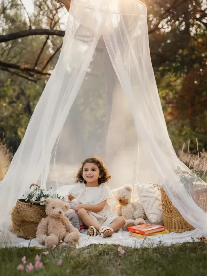 A toddler sits happily in her teepee tent during an outdoor photoshoot. The natural setting and props create a magical atmosphere.