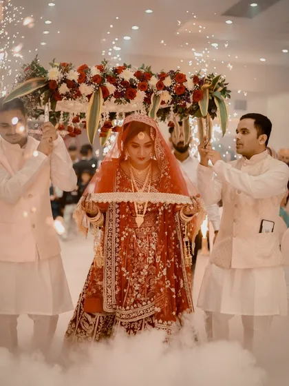 The bride's entry is a magical moment. I am so happy to see my bride looking absolutely radiant in a red lehenga, with makeup that glows even under the dramatic lighting and special effects of her grand entrance.