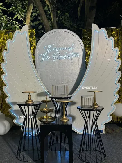 A stylish cake-cutting area for the rockstar party, featuring a backdrop with illuminated angel wings and a neon sign. This provided a cool, modern spot for photos.