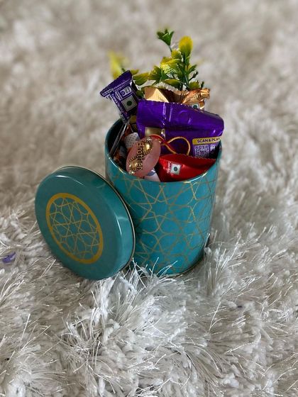 A compact and sweet Rakhi hamper. This decorative tin is filled with an assortment of chocolates and small treats, making it a simple yet heartfelt gesture for Raksha Bandhan.