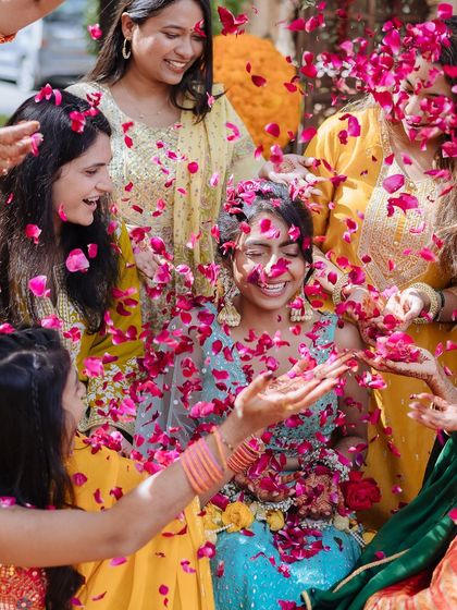 A bride's ecstatic laugh as she is showered with pink rose petals by her friends during her Udaipur Haldi.