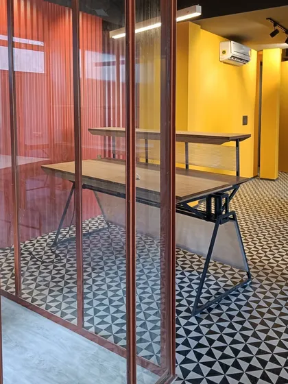 A glimpse into a private cabin in the New Delhi office, where a bright yellow accent wall and corrugated orange panels add vibrant pops of color to the industrial-modernist design.