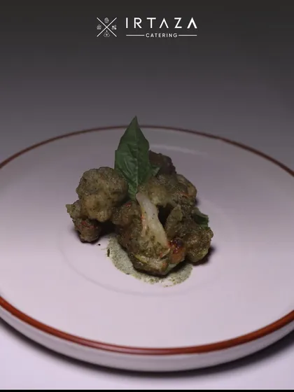 My signature herb-crusted cauliflower starter. The dish is delicately plated with a smear of green chutney and a fresh basil leaf, highlighting the fresh, earthy flavors.