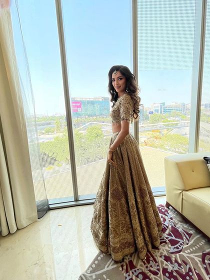 A full length shot of a client ready for an event. Her hair is styled in classic, voluminous waves that complement her golden lehenga.