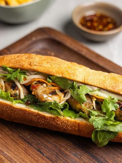 A close-up of the Plats Bánh Mì, showing the layers of fresh ingredients and savory grilled pork.
