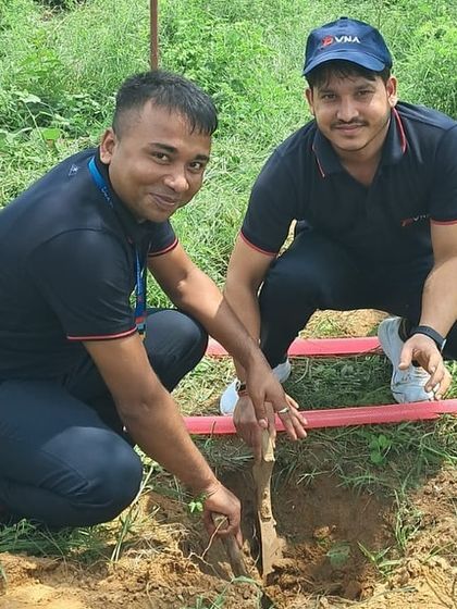 Two smiling volunteers from Padmini VNA plant a sapling together, contributing to the long-term health of the forest ecosystem.