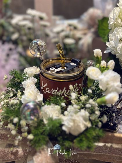 A personalized tumbler with the founder's name, 'Karishma', nestled in a bed of flowers.