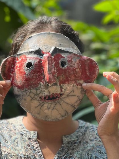 A student proudly displays a Raku mask made in our workshop. The red and white glaze with black crackles creates a powerful, expressive face.