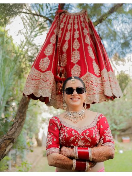 A cool and confident bride poses with sunglasses, her intricately embroidered lehenga skirt hanging from a tree behind her. This shot perfectly blends tradition with a modern, fun attitude.
