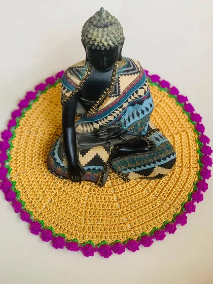 The yellow and lavender tulip doily styled with a Buddha statue, showing its versatility as a decorative mat.