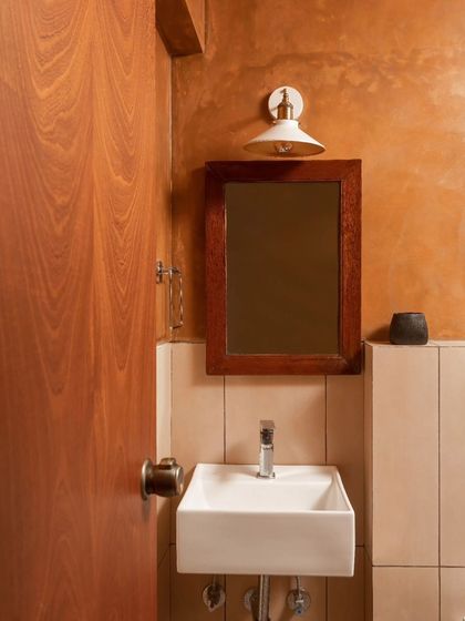 A detail of the powder room, highlighting the textured wall, wooden mirror frame, and minimalist fixtures that make the small space feel special.